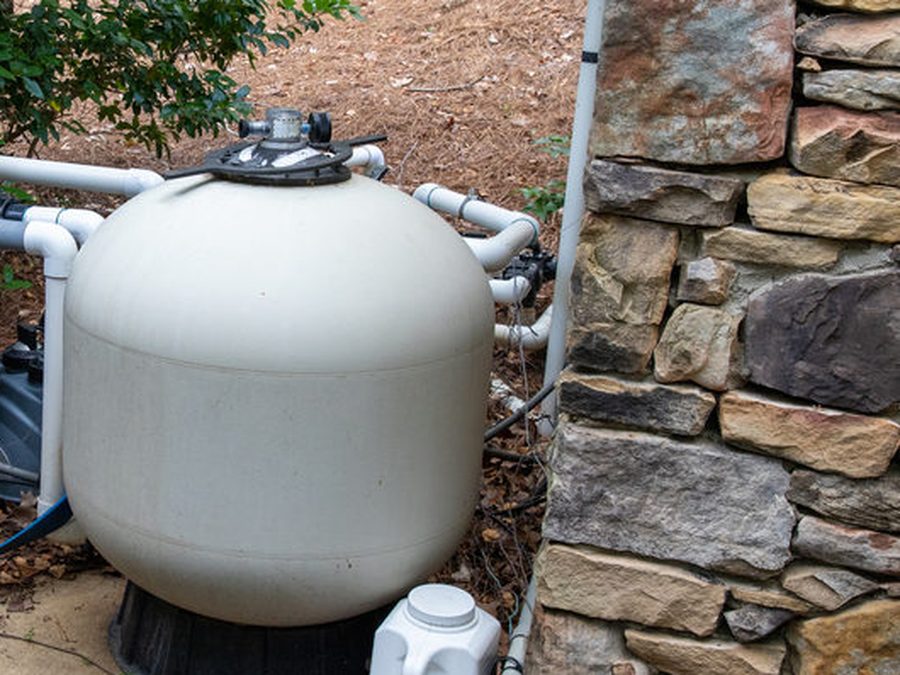 A sand filter tank and its multiport valve on a pool equipment pad